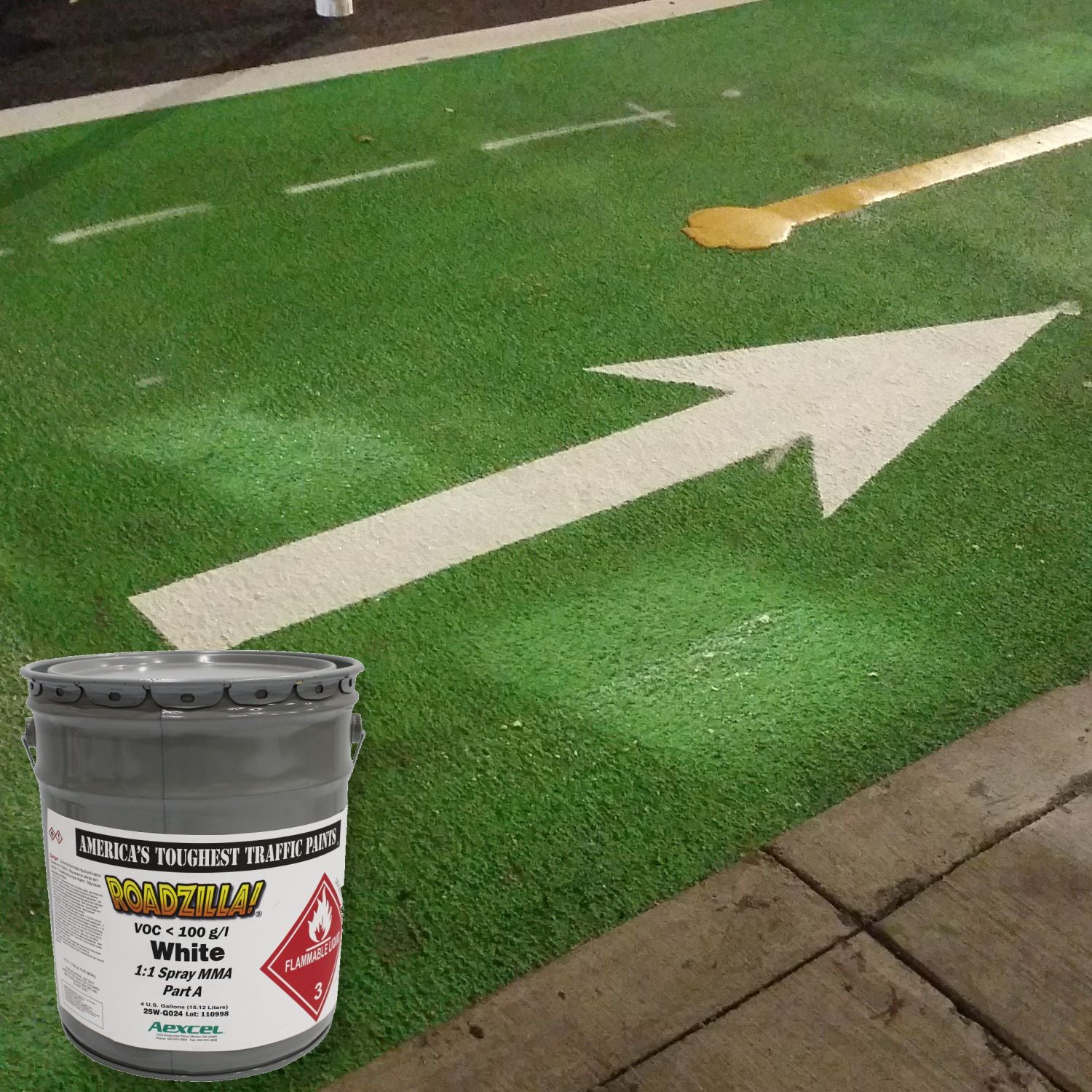 RoadZilla White MMA traffic marking paint displayed in front of a green bicycle lane featuring a white directional arrow and lane markings.